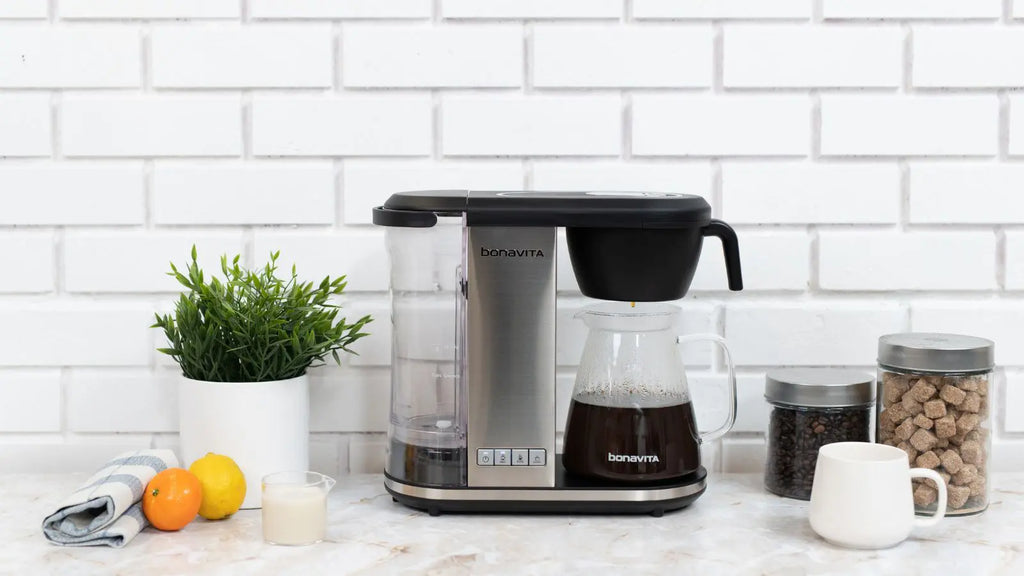 Bonavita Enthusiast glass coffee maker on a marble counter in front of a white brick wall.